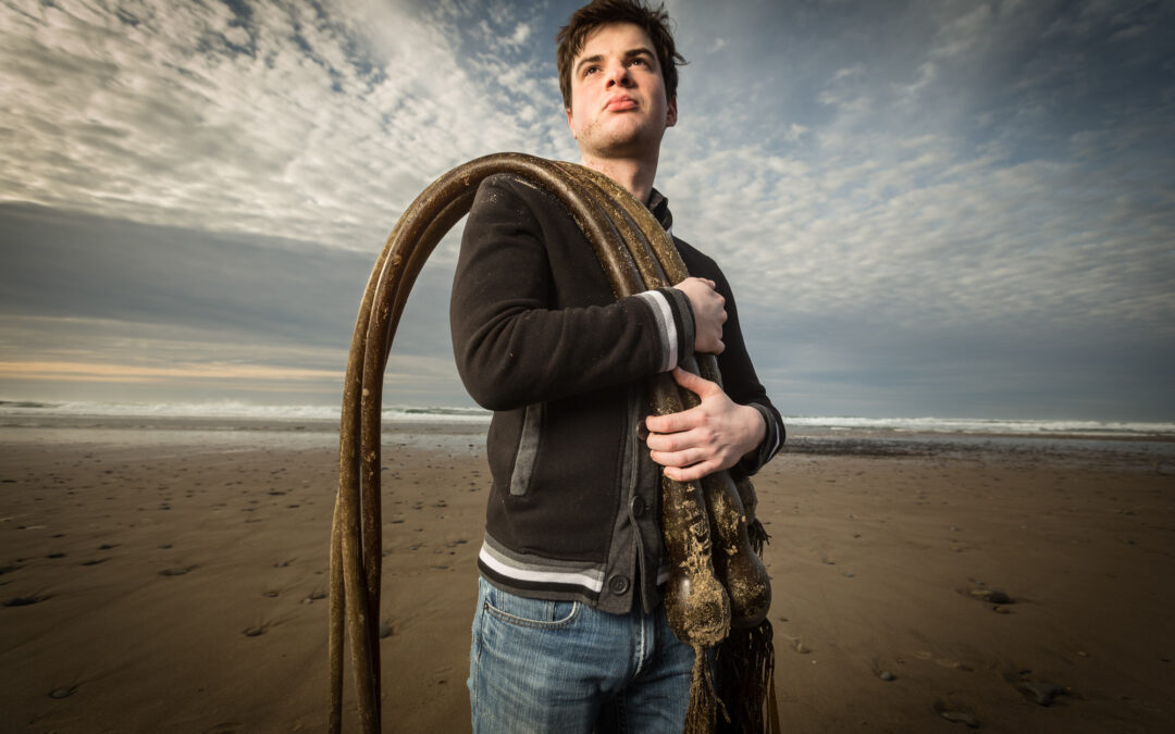 young man with serious look holding kelp over his shoulder on Oregon beach