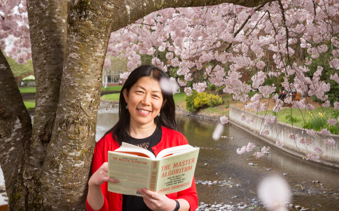 Asian woman standing next to cherry tree holding book and blossoms fall