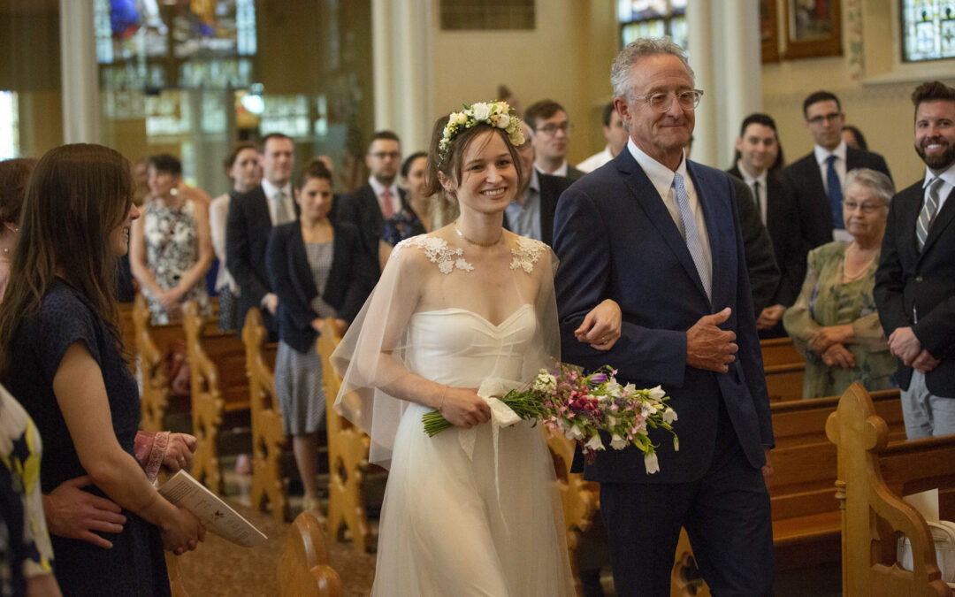 bride smiles at camera as her father leads her down the aisle