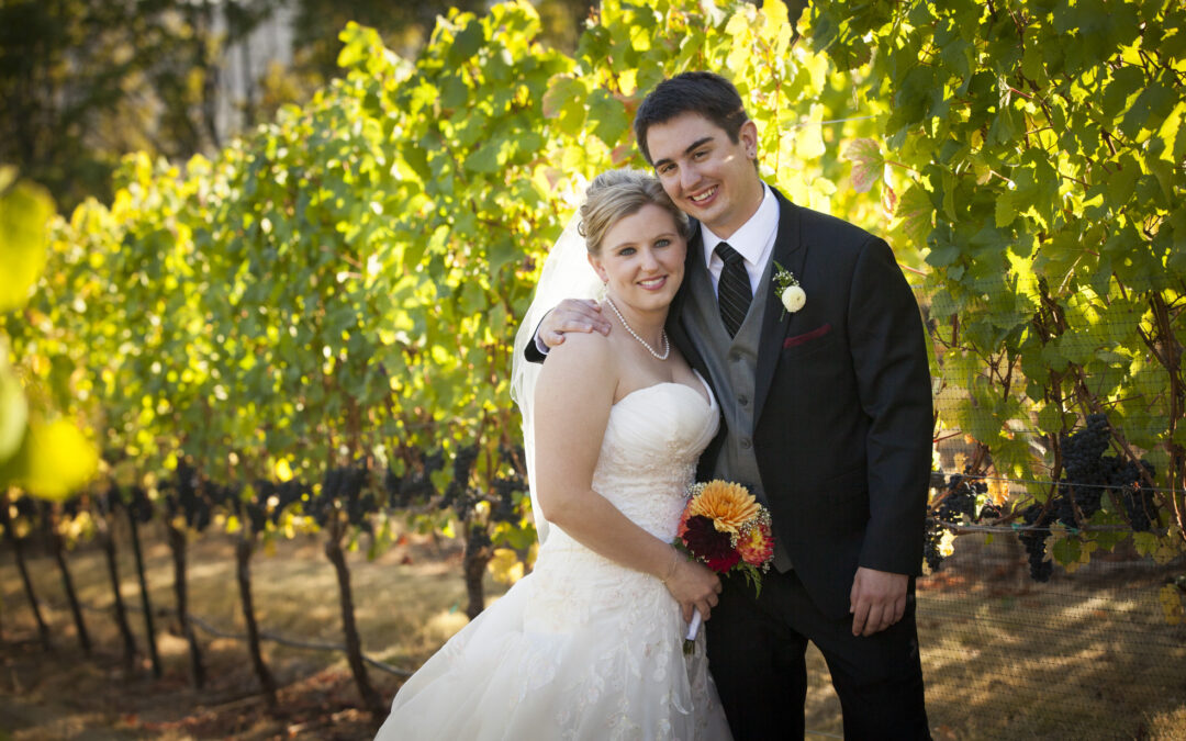 bride and groom cuddle among grape vines
