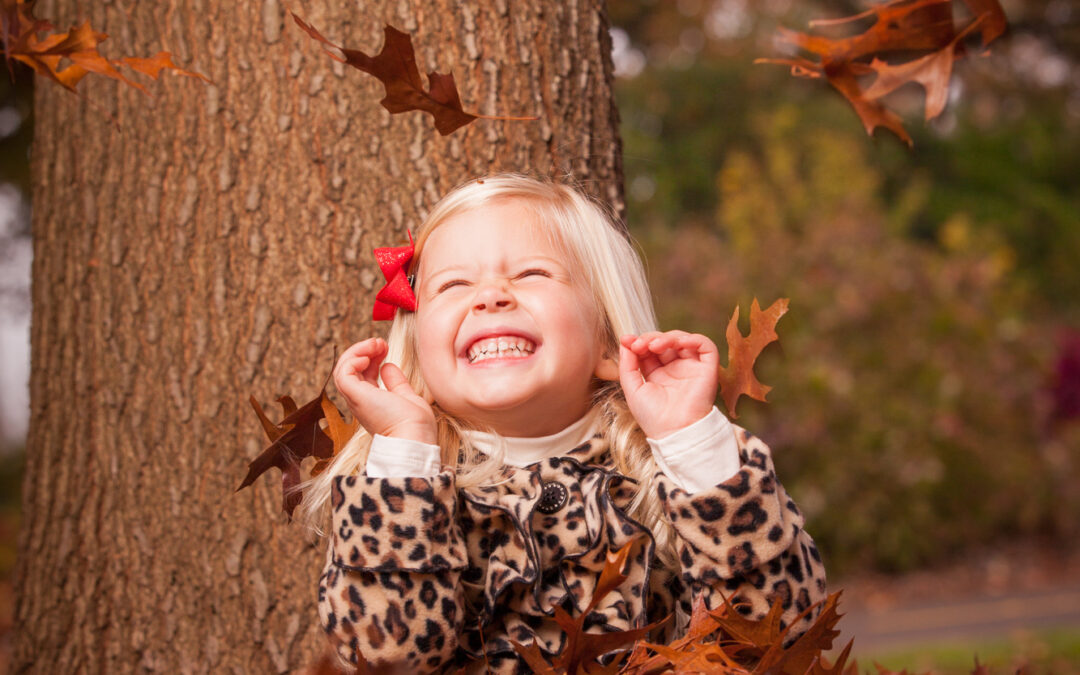 blonde girl jumps out from pile of autumn fall leaves