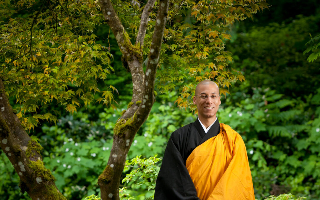 man in orange and black robe next to tree in wooded setting
