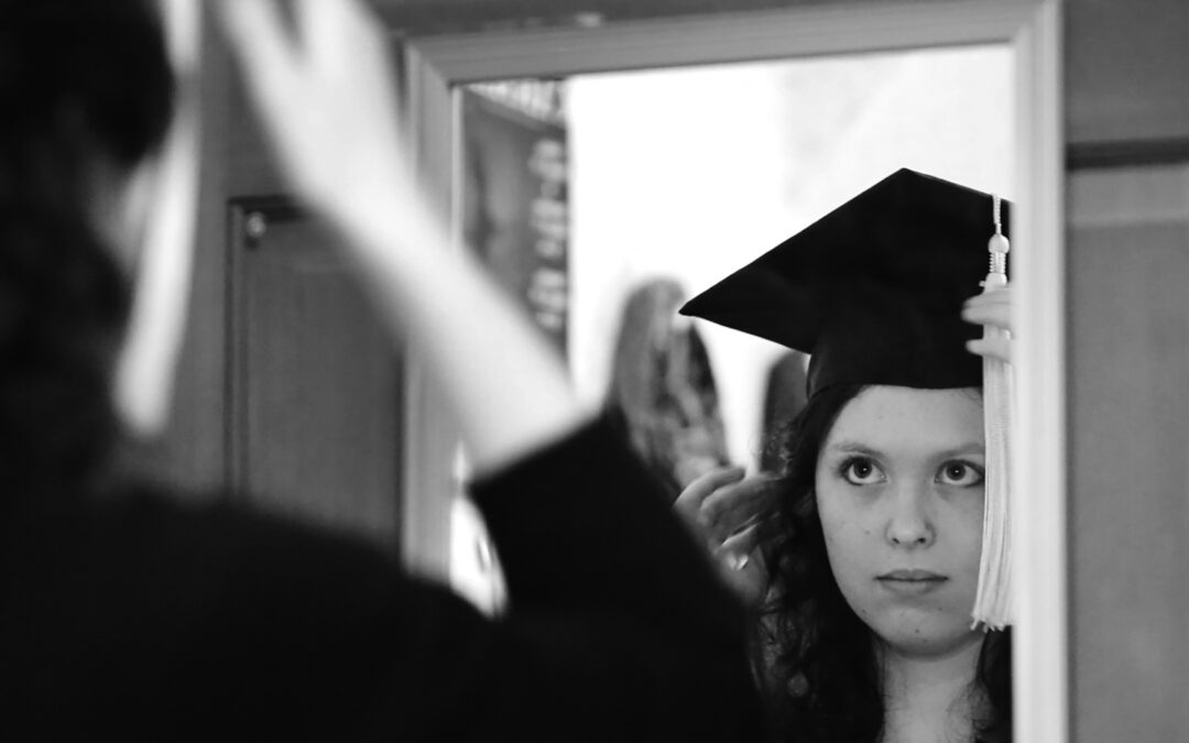 black and white image of young woman adjusting her mortarboard in a mirror