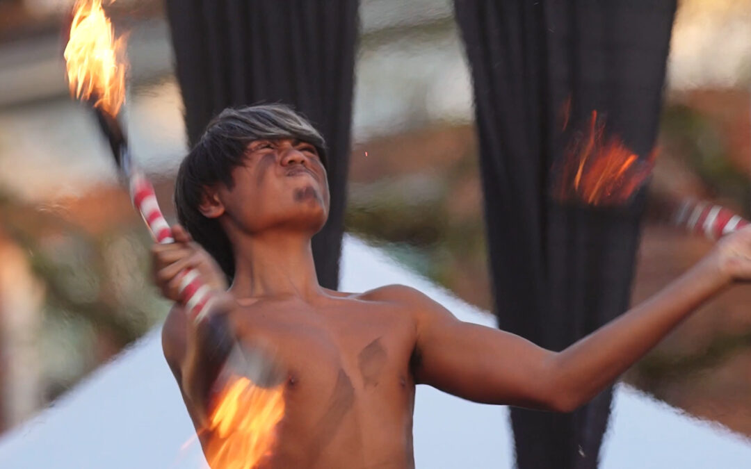shirtless Pacific Island young man spinning flaming batons