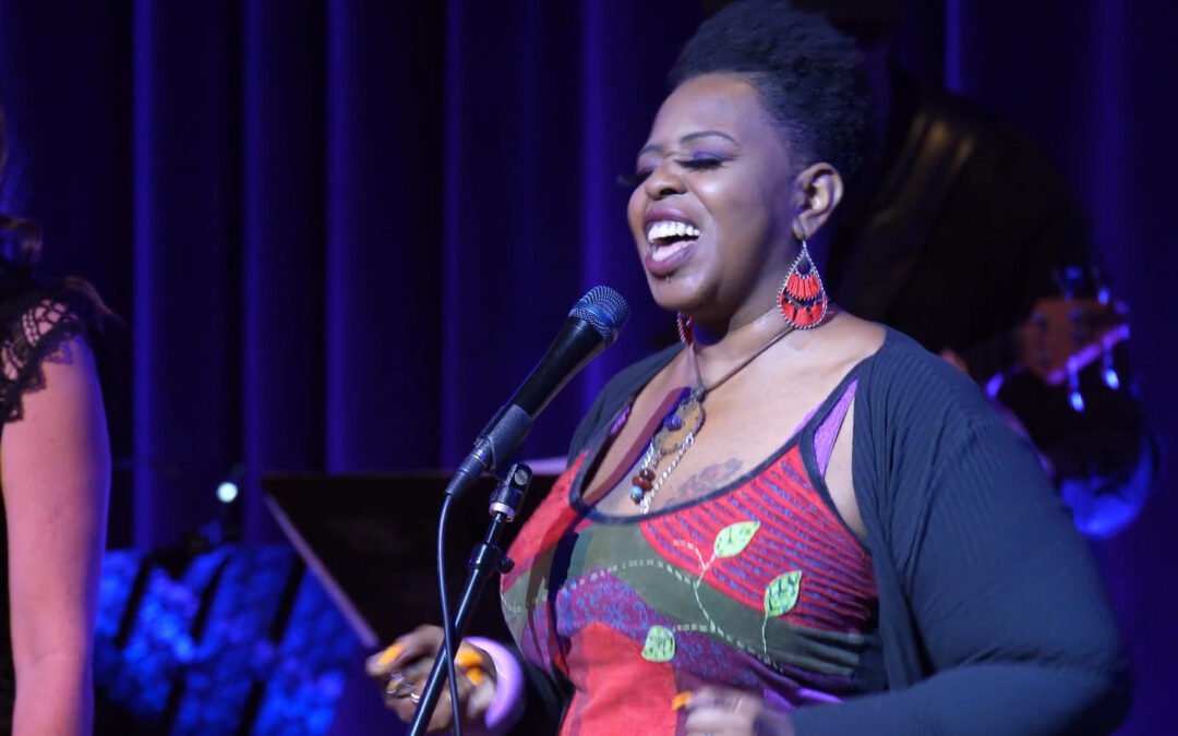 Black woman singing on stage with musicians in background